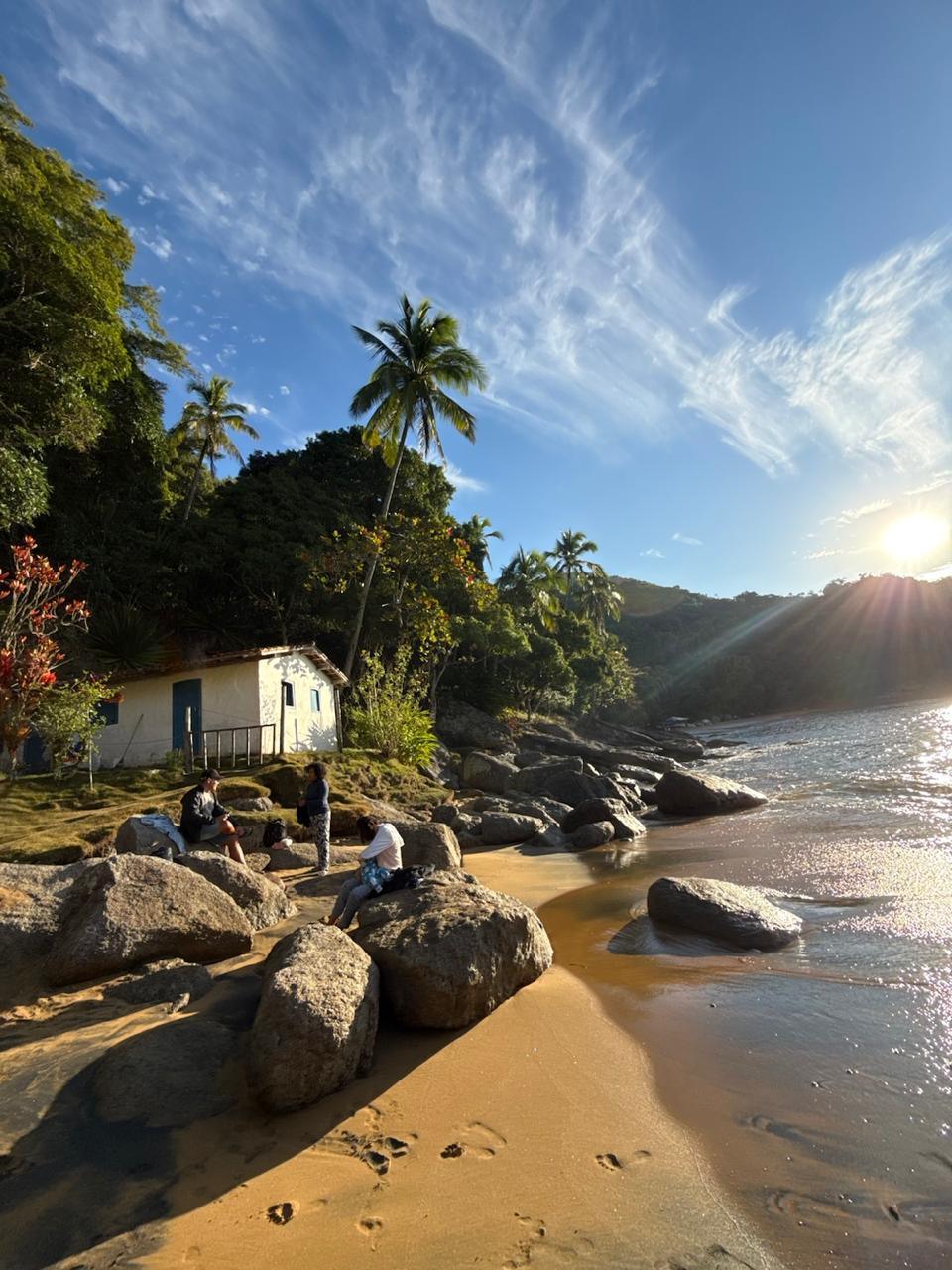 Praia com casa de pescador ao fim de tarde, grupo descansando à beira-mar em Ilhabela
