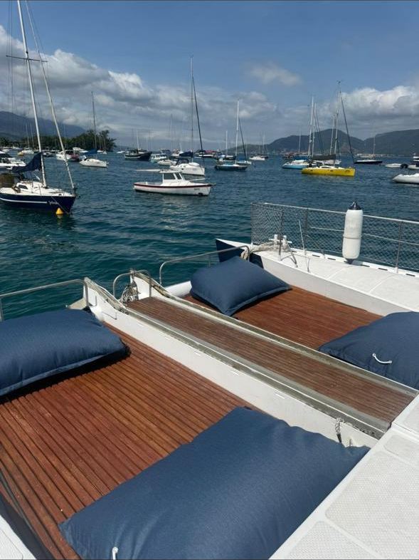 Deck de madeira do catamara com almofadas azuis - vista da baia com veleiros ao fundo