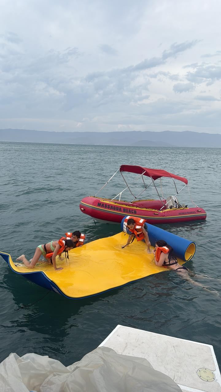 Passageiros brincando em boia flutuante amarela com barco de apoio - atividades a bordo