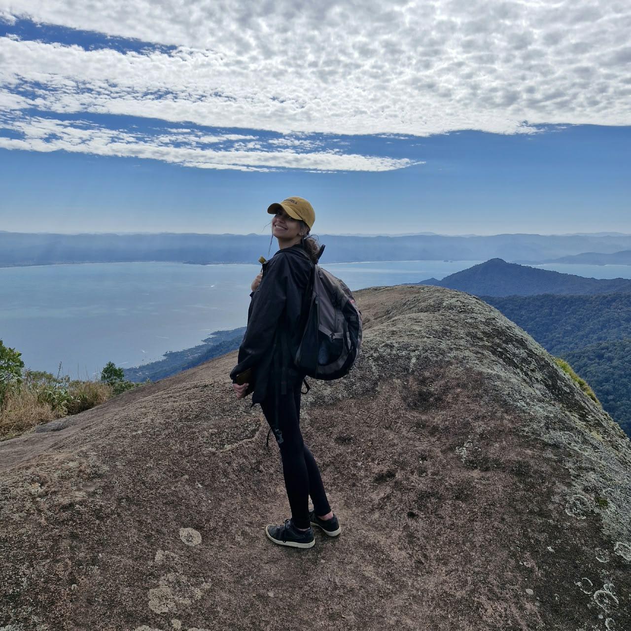 Aventureira sorrindo no cume do Pico do Baepi com vista panoramica de Ilhabela ao fundo