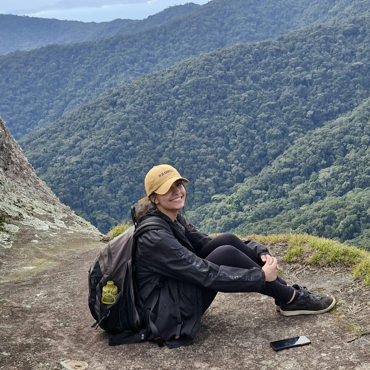 Aventureira sentada com bone Ilhabela contemplando a mata atlantica e vales do Pico do Baepi